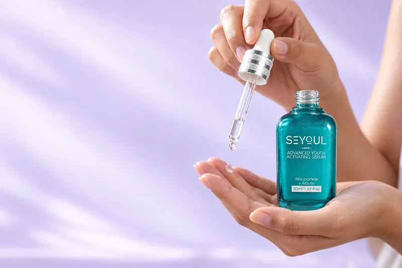 Hands pressing drops of serum onto the skin